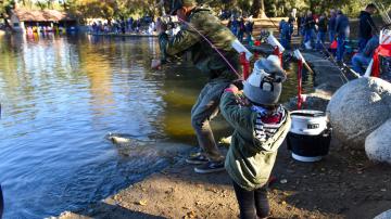 Child by a lake catching a fish with a parent's help