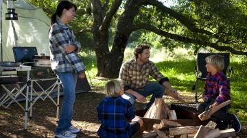 Family around a fire ring in front of a tent