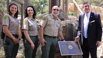 Three OC Zoo staff and OC Supervisor Donald P. Wagner stand next to a plaque commemorating the opening of the new OC Zoo large mammal exhibit.