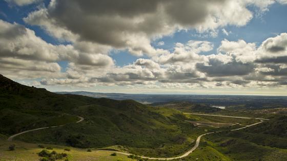 Rolling green hills with a winding road under blue sky and puffy clouds