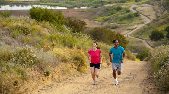 Man and woman jogging up a trail with a lake in the background