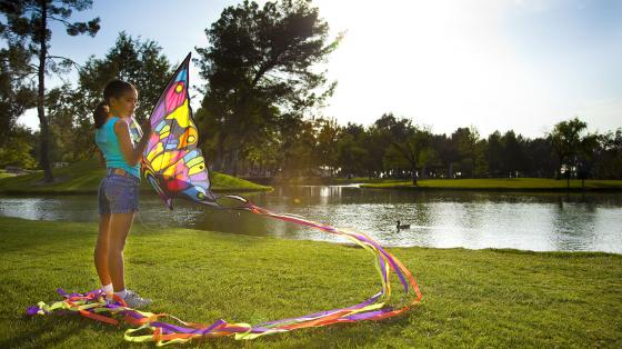 Child holding a colorful kite on a grassy area next to a lake
