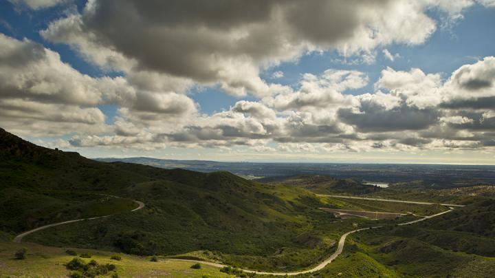 Rolling green hills with a winding road under blue sky and puffy clouds