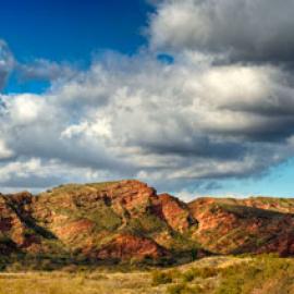 Red-hued cliffs under a blue sky with puffy clouds