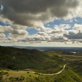 Rolling green hills with a winding road under blue sky and puffy clouds