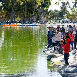 Crowd of children fishing along the side of a small lake