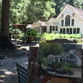 Small painting of the home at Arden on an easel, the real house can be seen behind it.