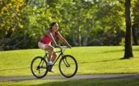 Woman riding a bike on a trail through green grass at the park