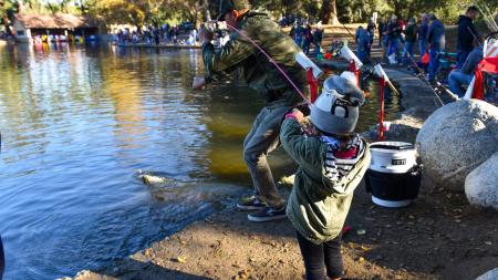 Child by a lake catching a fish with a parent's help