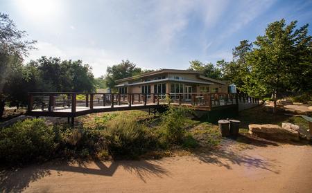 Modern-looking visitor center building with a wooden deck amid sage scrub under a blue sky