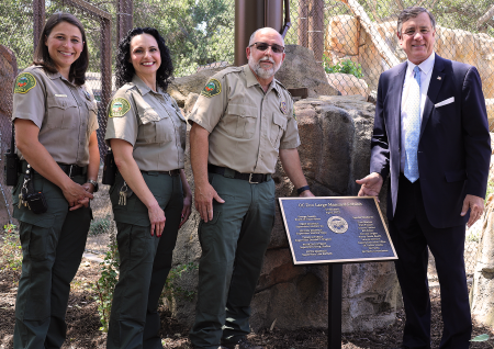 Three OC Zoo staff and OC Supervisor Donald P. Wagner stand next to a plaque commemorating the opening of the new OC Zoo large mammal exhibit.