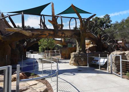 Pathway under an enclosed bridge that links two rustic-looking animal enclosures